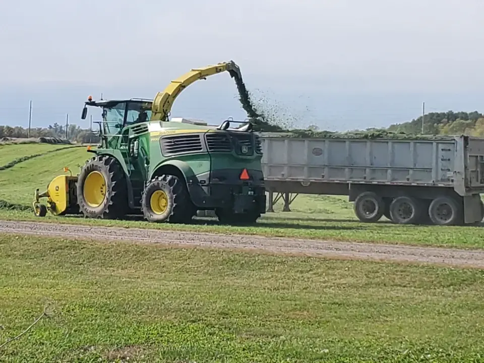 Farm machinery harvesting a field alongside a wagon