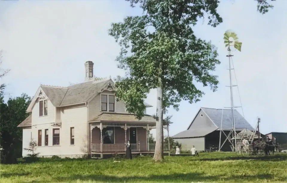 Older photograph of the white farmhouse with a tree and outbuilding