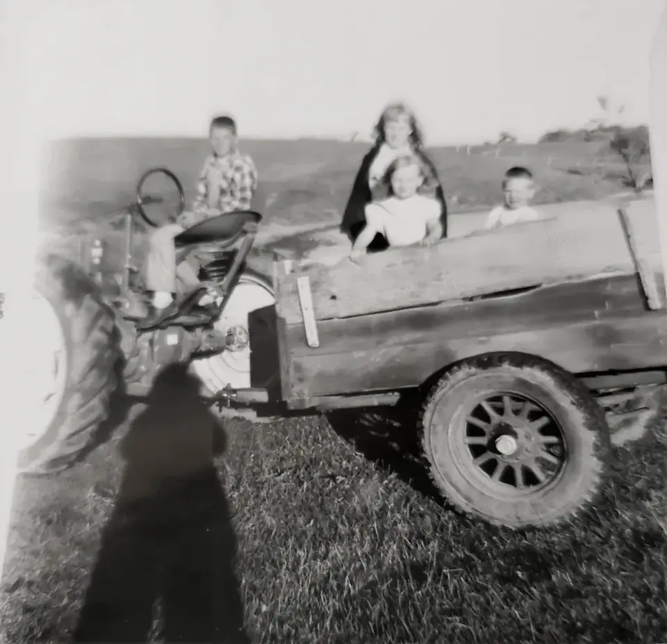 Archival photograph of family members riding on a tractor and farm wagon